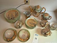 Overview of tea set items including teapot, creamer, sugar bowl, stacked plates, cups and saucers showing handpainted cherry blossom decoration and gold accents.