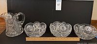 Set of three large cut crystal serving bowls with scalloped edges and one large cut crystal pitcher on a black surface with ruler for scale.