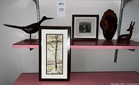Shelf display showing all four items: wood carved shore bird, gazelle figurine, painted wood slice wall hanging, and framed watercolor painting on shelf.