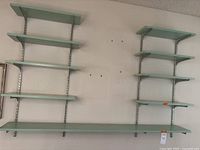 Two wall-mounted shelving units with light sage green painted wood shelves supported by metal brackets and vertical rails.