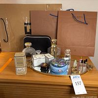 Mirror tray on wooden surface holding assorted perfume-related items and high-end paper shopping bags in background