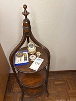 Full view of round three-tier wooden display table with finial top and displayed items