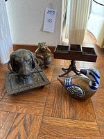 Overview of all four items arranged on wood floor: ceramic and brass duck, dog head inkwell, pedestal table with brass inserts, metal bear figurine