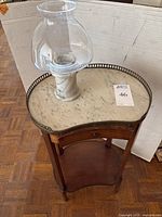 Full view of Victorian curved wooden table with marble top and metal lip with carved marble candle base and glass hurricane top placed on it