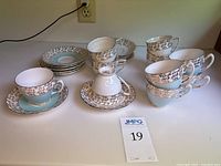 Full display of 10 teacups with white and turquoise saucers arranged on counter.