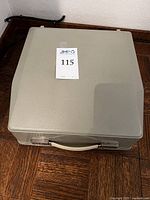 Closed hard plastic carrying case in sea foam green with carry handle and lot label