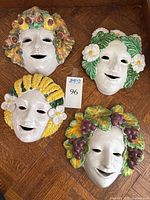 Front view of four masks laid on wood floor showing colored wreaths
