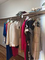 Photo of women's clothing on hangers and rack including colored jackets, sweaters, skirts, and dresses with visible label tags showing variety of styles and colors.