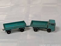 Green die cast truck and trailer connected, showing side profile with flatbed areas and wheels.