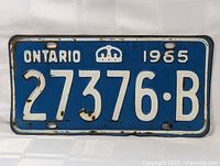 Full view of the 1965 Ontario license plate showing the complete number 27376-B, with visible rust spots and paint wear around edges and mounting holes.