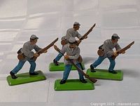 Four Britains Confederate Soldier metal toy figures arranged standing and aiming rifles. Shown on white surface.