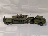Side view of green military transport truck with camouflage tank on trailer bed.