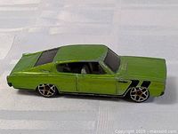 Side profile view of green Hot Wheels Dodge Charger diecast model showing paint wear and black stripes on front fenders