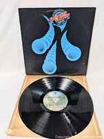 Photo showing the vinyl LP record partially pulled out of the album sleeve. The label on the record is visible and the cover art is predominantly black with blue graphics and title text.