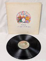 Vinyl record layed flat with visible label and associated album cover in background.