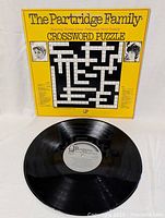 The Partridge Family Crossword Puzzle vinyl record displayed with front cover showing the yellow crossword puzzle design and images of Shirley Jones and David Cassidy.