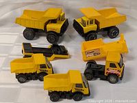 Five vintage yellow construction toy trucks displayed on white cloth, including Tonka and Buddy L trucks in various sizes.