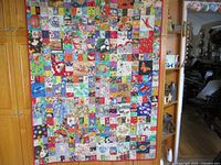Full view of the quilt hanging, showing the colorful patchwork composed of many small fabric squares with various patterns and images