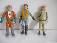 Front view of three Ghostbusters action figures standing upright on a white background, showcasing colors, attire, and details of each figure.