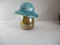 Side view of the art glass toadstool paperweight showing blue-green cap and brown base.