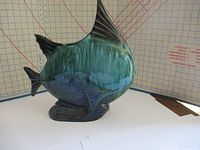 Front view of the blue and green glazed angel fish sculpture showing the detailed fins and eye, on a patterned background with measurement grid.