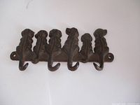 Front view of cast iron dog key holder showing five dog-shaped hooks in a row on a flat mounting base with holes on each side for wall attachment.