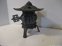 Side view of the cast iron pagoda-style lantern showing the hinged door open and the three-legged base.