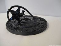 Close-up view of the black cast iron sun dial showing the star-shaped gnomon and Roman numerals on the dial plate.