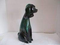 Side view of a hairless dog ceramic figurine, showing glossy green and black finish, large eyes and floppy ears.