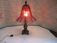 Full view of cranberry glass table lamp illuminated, showing shape and light quality