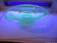 Side view of etched uranium glass bowl glowing bright green under UV light.