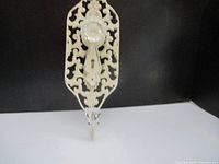 Front and side views of wall-mounted coat hanger with cream metal ornate backplate, clear glass knob, and metal hook.