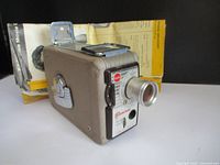 Angled view of Kodak Brownie camera showing lens, body, and instruction manual in background.