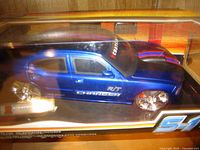 Blue Dodge Charger R/T remote control car inside clear display box with yellow and black trim, showing side profile.