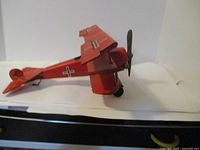 Side view of the red metal biplane model showing the left side wing, fuselage, tail, and propeller details.