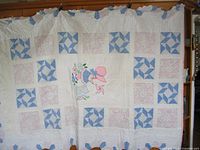 Full view of the quilt hung up showing alternating blue pinwheel and pink floral patchwork blocks with a white base.