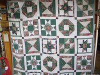 Full view of quilt displaying multiple types of patchwork blocks with stars and floral motifs in green, pink, white, and blue fabric.