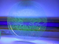 Top view of the 8.5-inch uranium glass plate glowing bright green under UV light showing etched decorative pattern.