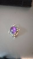 Oval cabochon amethyst in silver setting with decorative bead details, hanging bail visible.