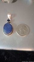 Front angle of the pendant next to a quarter, showing the blue oval and round sapphires and silver setting.