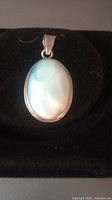 Front view of oval blue aragonite stone pendant set in silver on black background