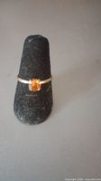 Photo showing the antique gold ring with a rectangular tangerine stone set on a black cone display.