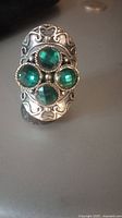Close-up front view of the antique silver tone statement ring with four green faceted stones, showing ornate detailing and size compared to a coin.
