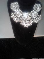Clear rhinestone bib collar necklace displayed on a black bust stand, showing the intricate clustered arrangement of rhinestones in various cuts forming a floral design.