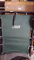 Green Coleman Ridgeline camping cot folded showing top fabric surface with Coleman logo and metal frame.