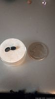 Two oval blue sapphire gemstones displayed on a white base next to a quarter coin for scale.