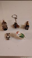 Lot overview showing all five miniature vintage collectibles including the decorative bottle, bear clock, baby cradle, keychain, and miniature bottle replica.