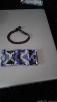 Two bracelets on flat surface: a wide Native American style blue, white, black beaded cuff bracelet and a smaller black beaded cuff bracelet with clasp