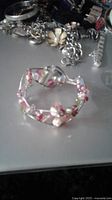 Photo showing sterling silver cuff bracelet with pink pearls and red/pink stones on a gray surface among other jewelry pieces
