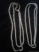 Two lengthy pearl necklaces laid on a black textured background, showing size and uniformity of pearls.
